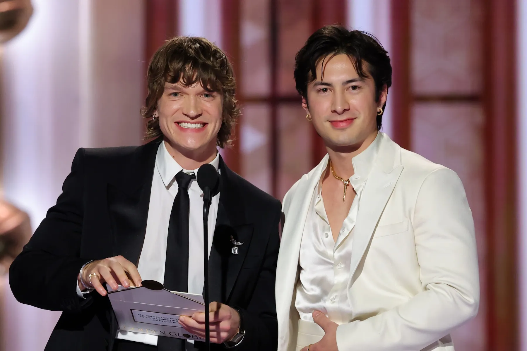 'Heated Rivalry' stars Connor Storrie and Hudson Williams smiling while on stage presenting at the 2026 Golden Globes