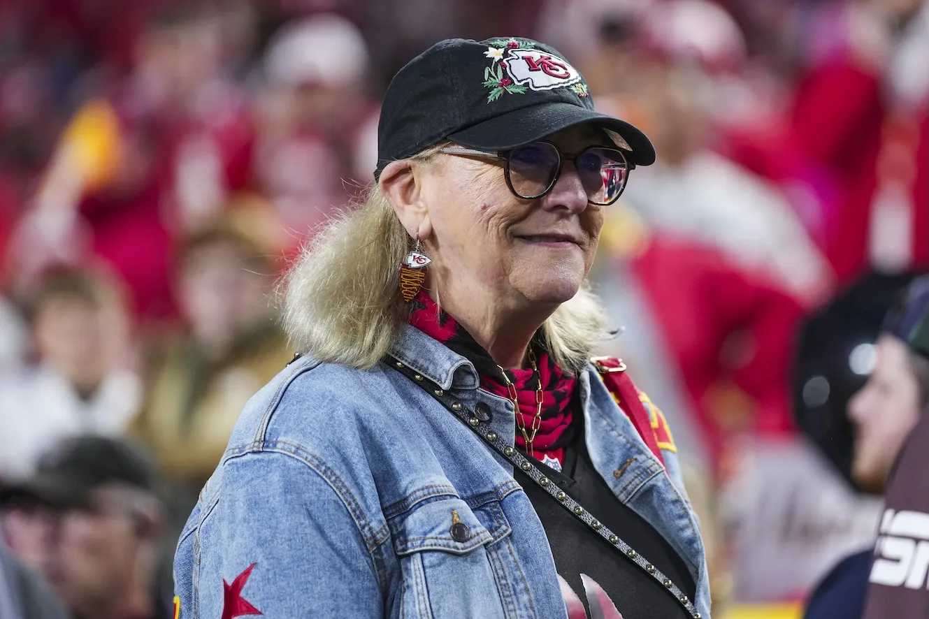 A side view of Donna KElce at an NFL game. She's wearing a baseball cap and denim jacket.