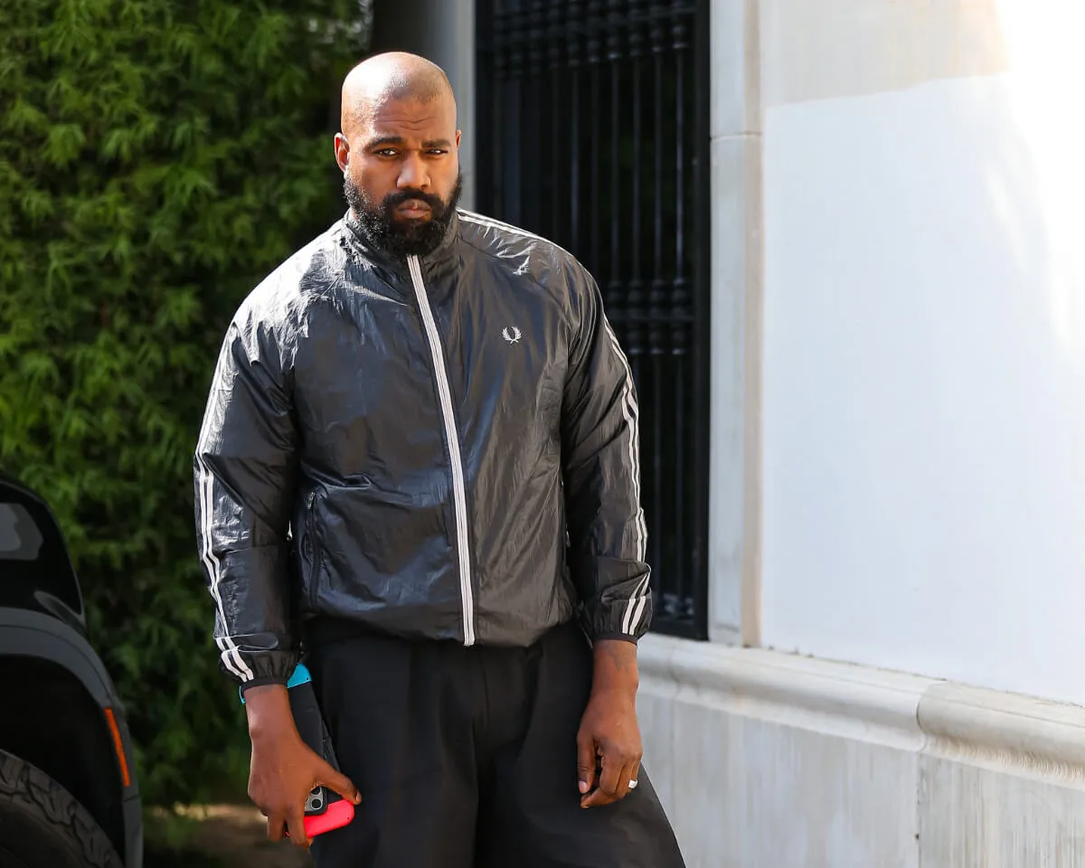 Kanye West wears a black jacket and stands outside.