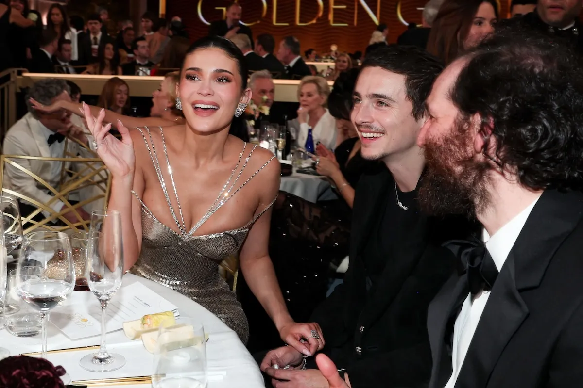 Kylie Jenner smiling mid-sentence with Timothée Chalamet looking forward and smiling while they sit at a table at the Golden Globes