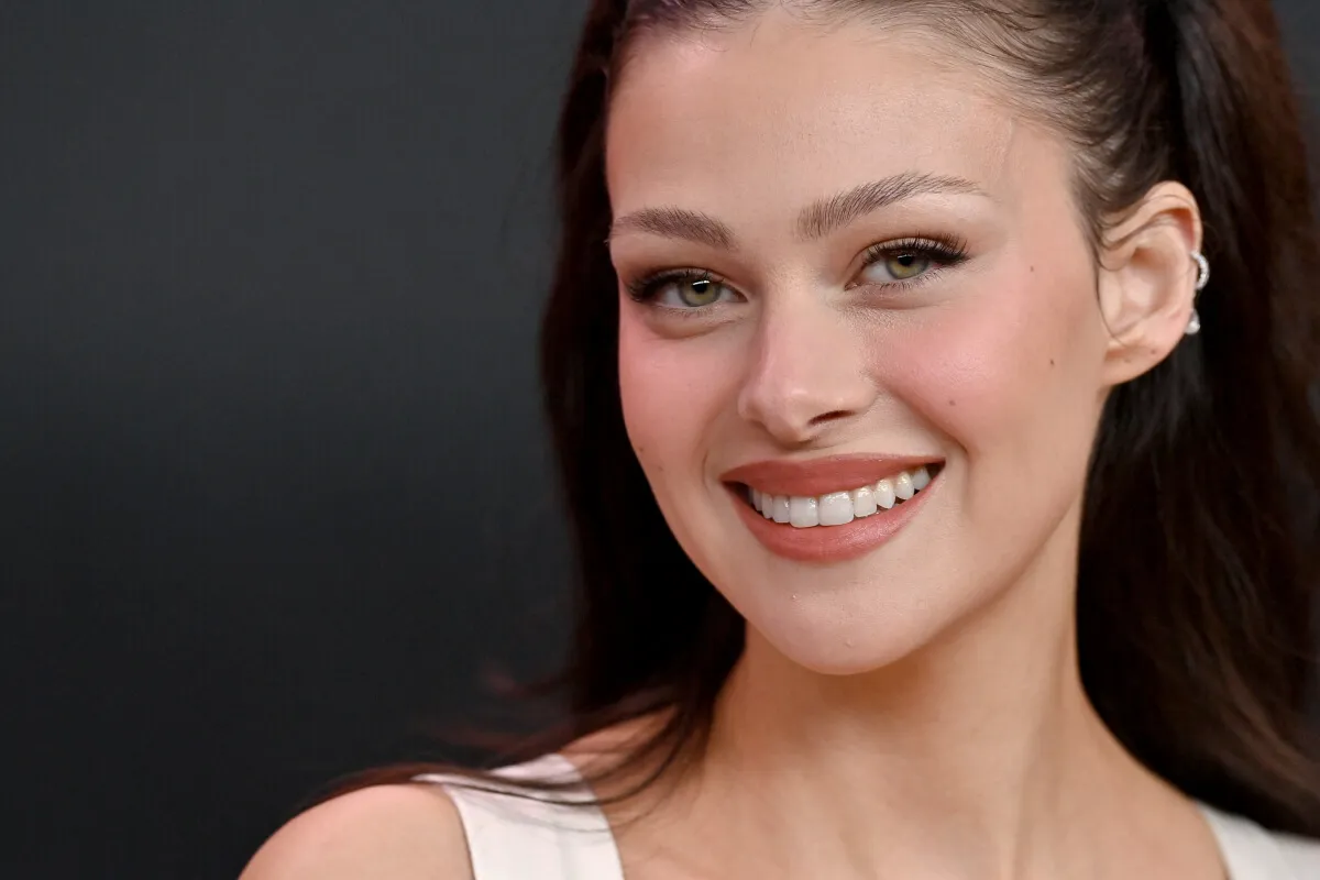 Nicola Peltz smiles and wears a white tank top.