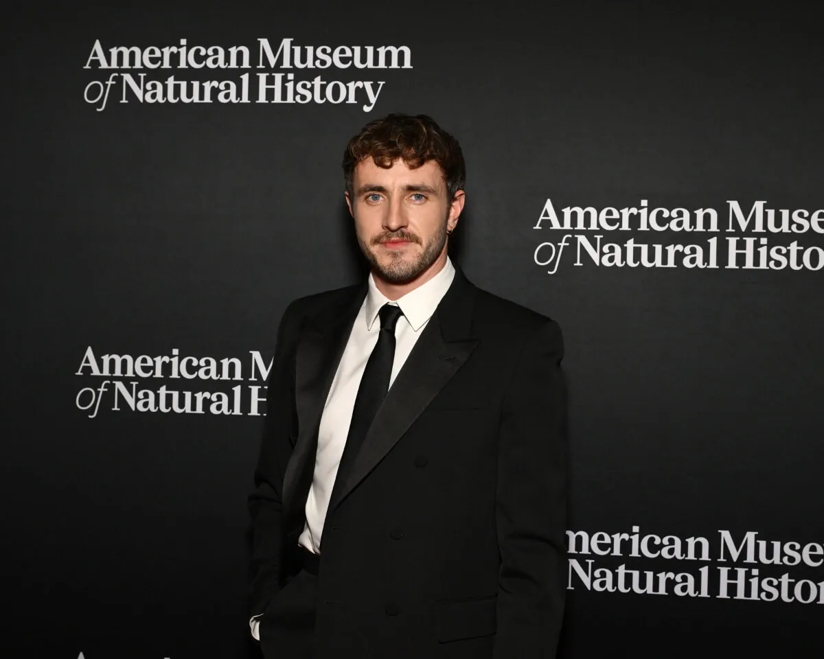 Paul Mescal wears a suit and stands in front of signage for the American Museum of Natural History.