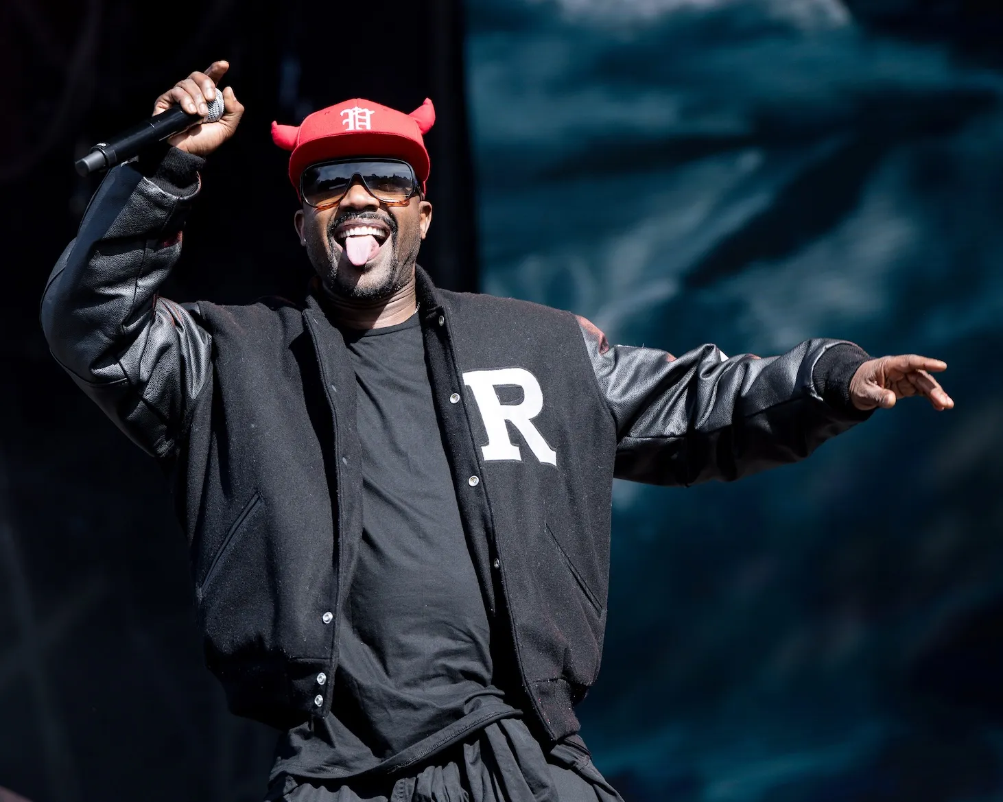 Ray J holding a microphone onstage while sticking his tongue out. He's wearing a red hat and sunglasses.