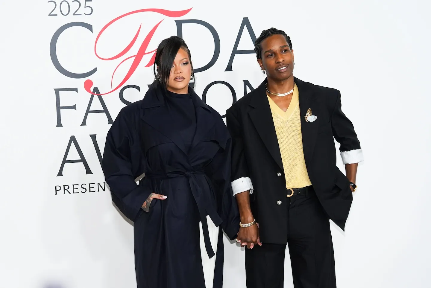 Rihanna in a black outfit posing with A$AP Rocky who's in a black suit jacket and matching pants at an event in 2025
