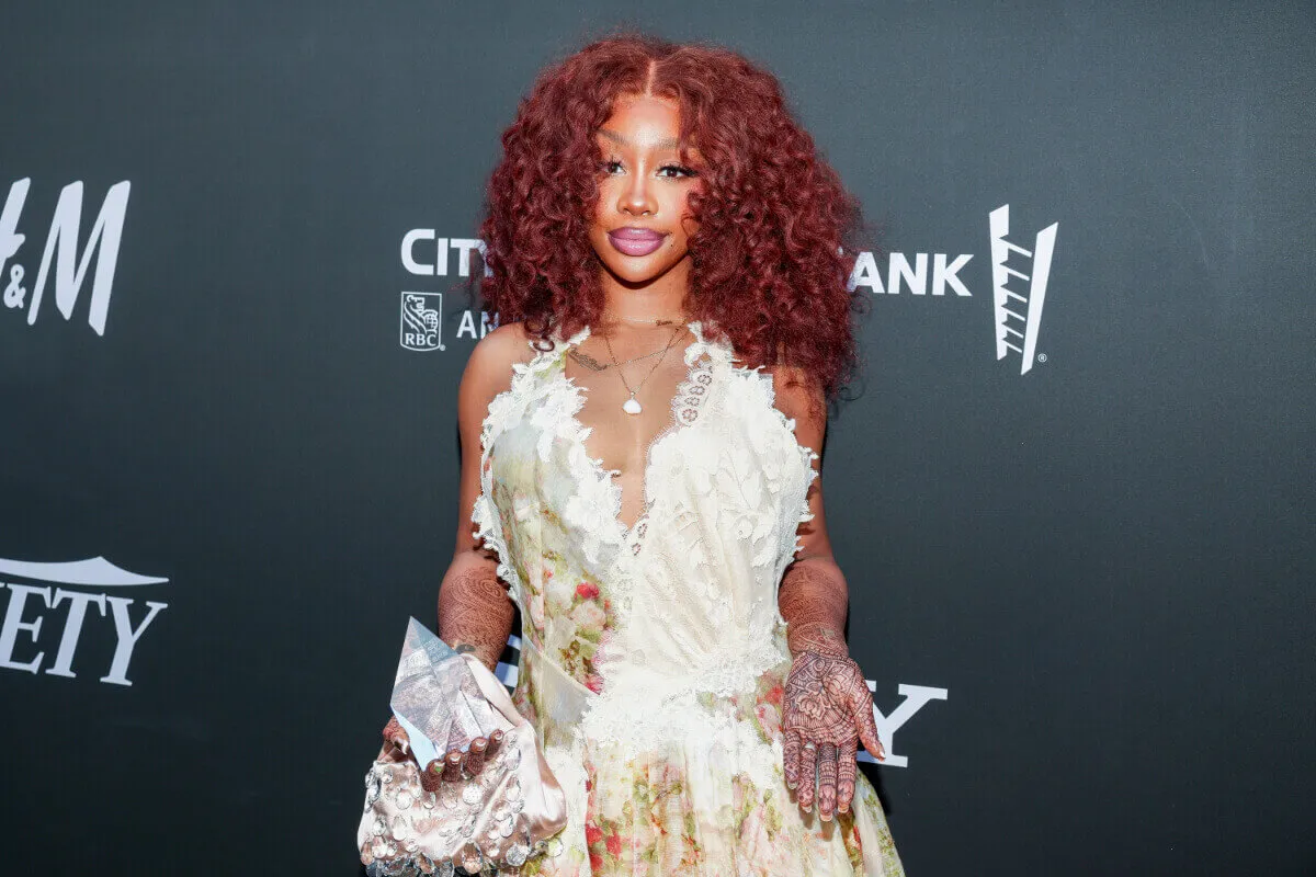 SZA wears a floral dress and stands on a red carpet.