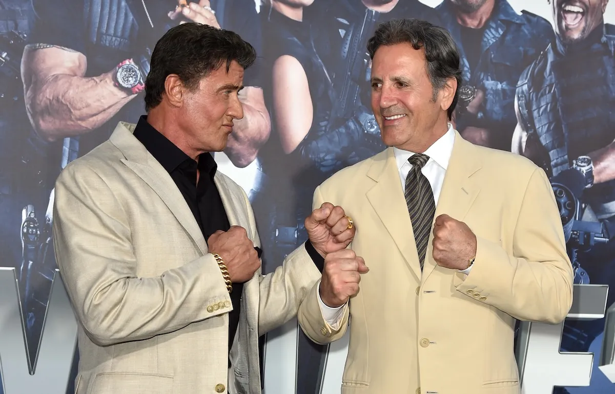 Frank and Sylvester Stallone playfully posing like they're going to box each other at a movie premiere in 2014. They're wearing light-colored suit jackets.