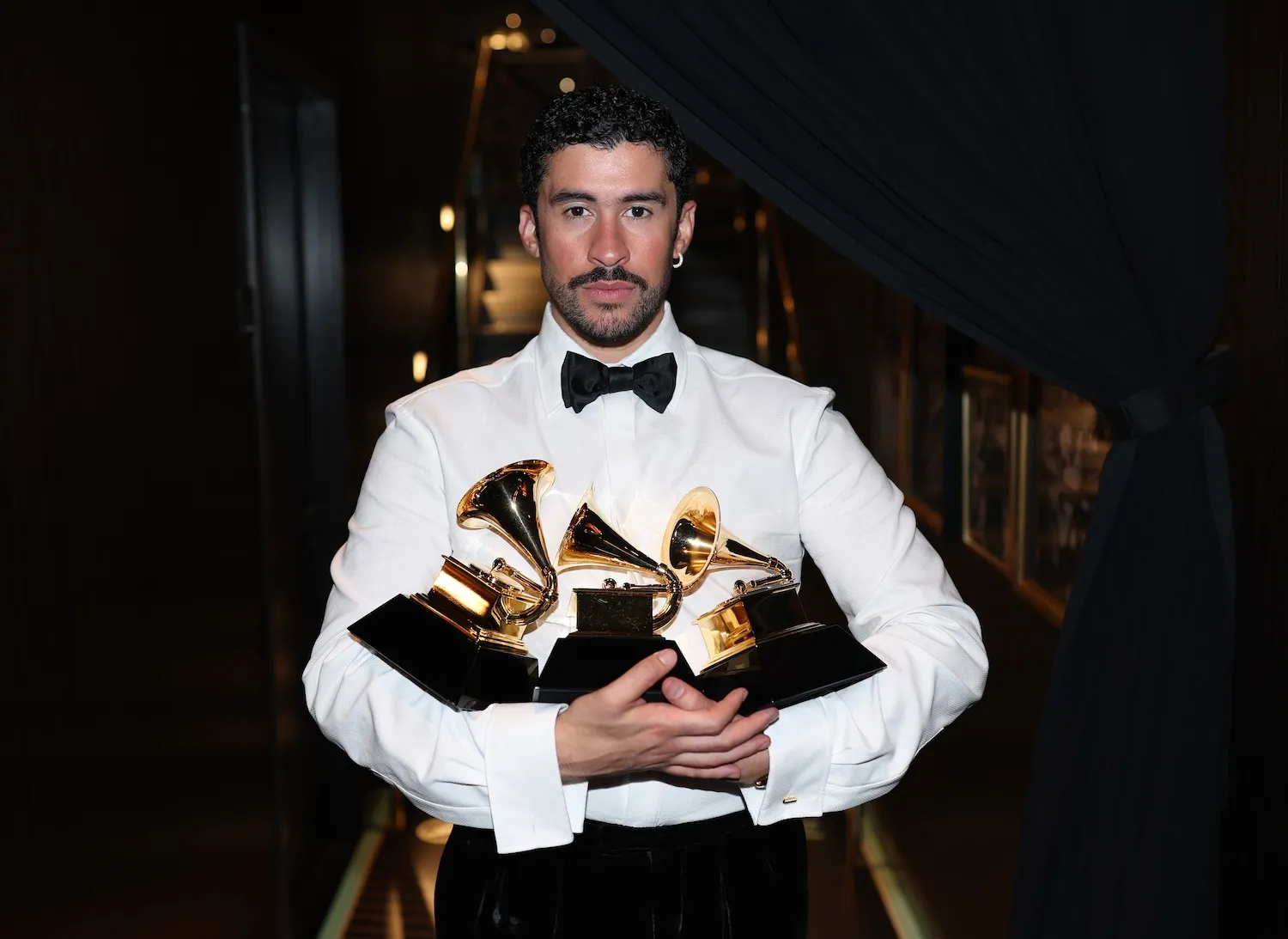 Bad Bunny in his tuxedo shirt and a bow tie while holding multiple Grammy Awards in 2026