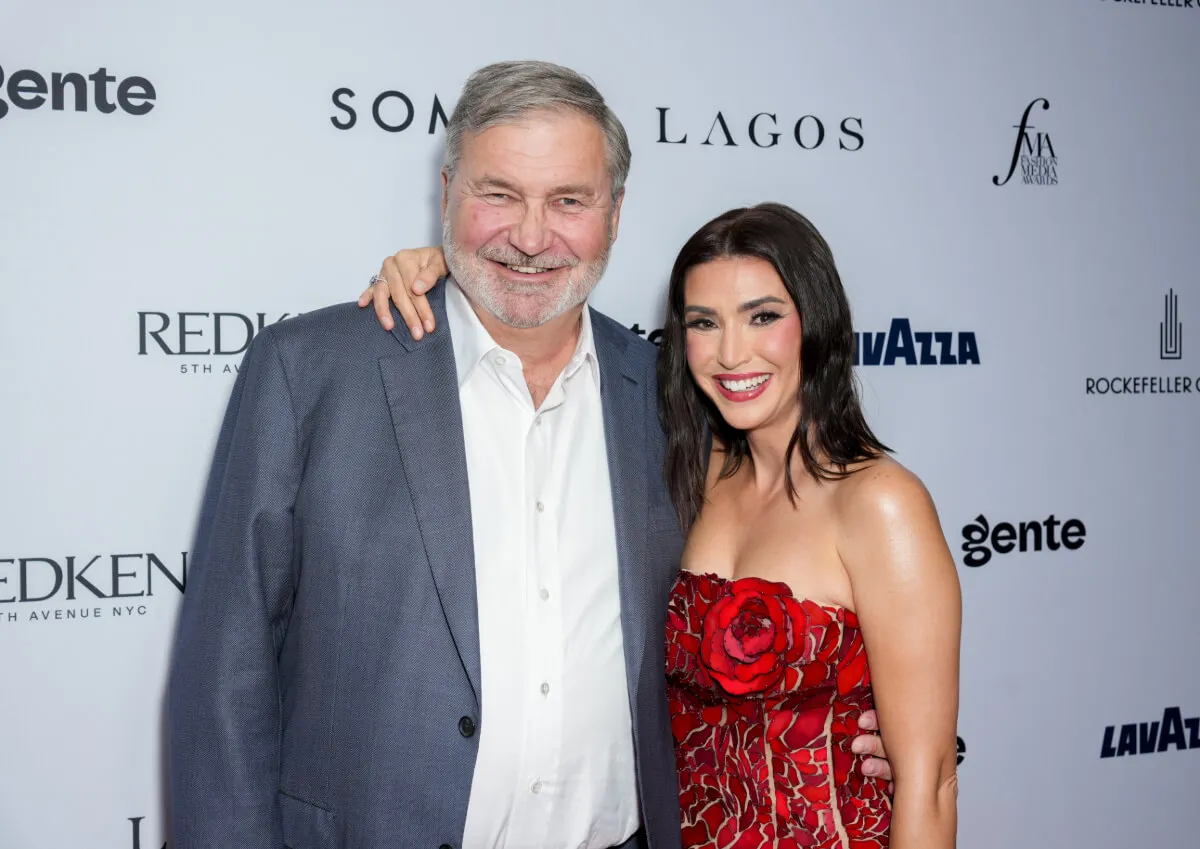 Bronwyn Newport wears a red dress and stands with her arm around Todd Bradley's shoulders. He wears a gray suit.
