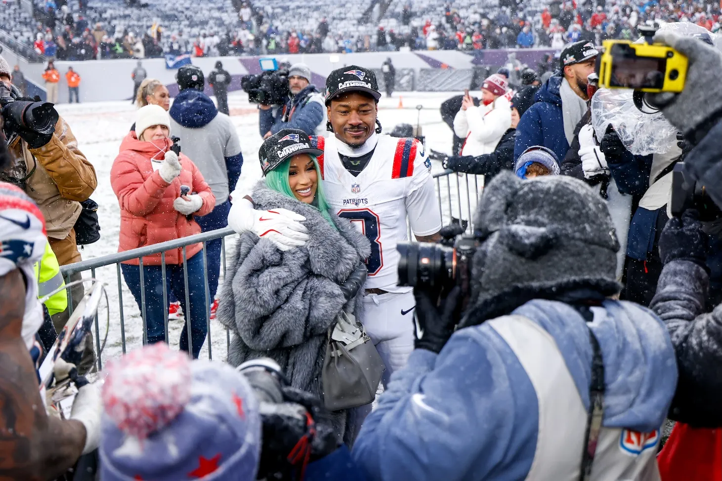 Cardi B and Stefon Diggs posing together after the AFC Championship game. There are crowds around them outdoors.
