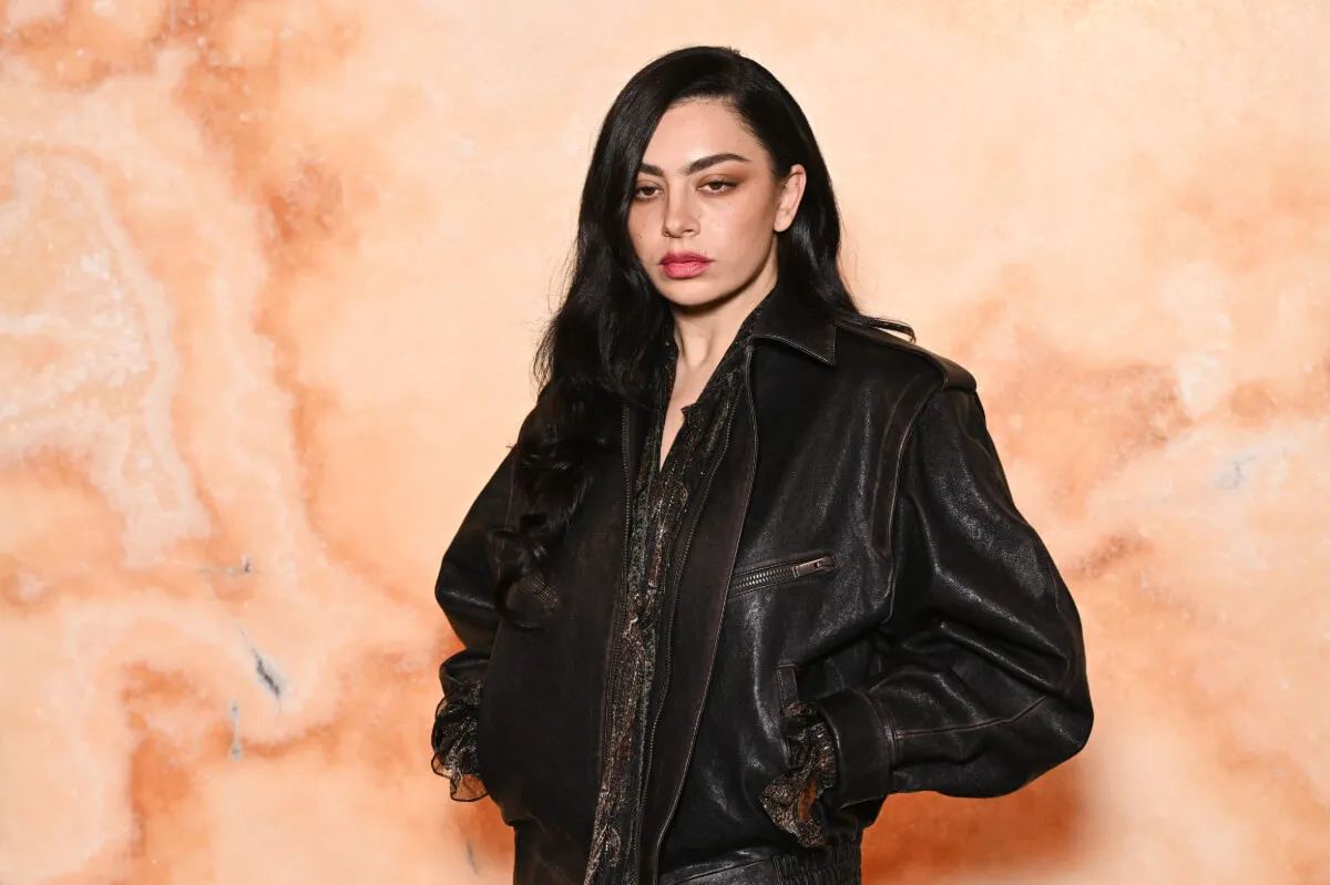 Charli xcx wears a black leather jacket and stands with her hands in her pockets.