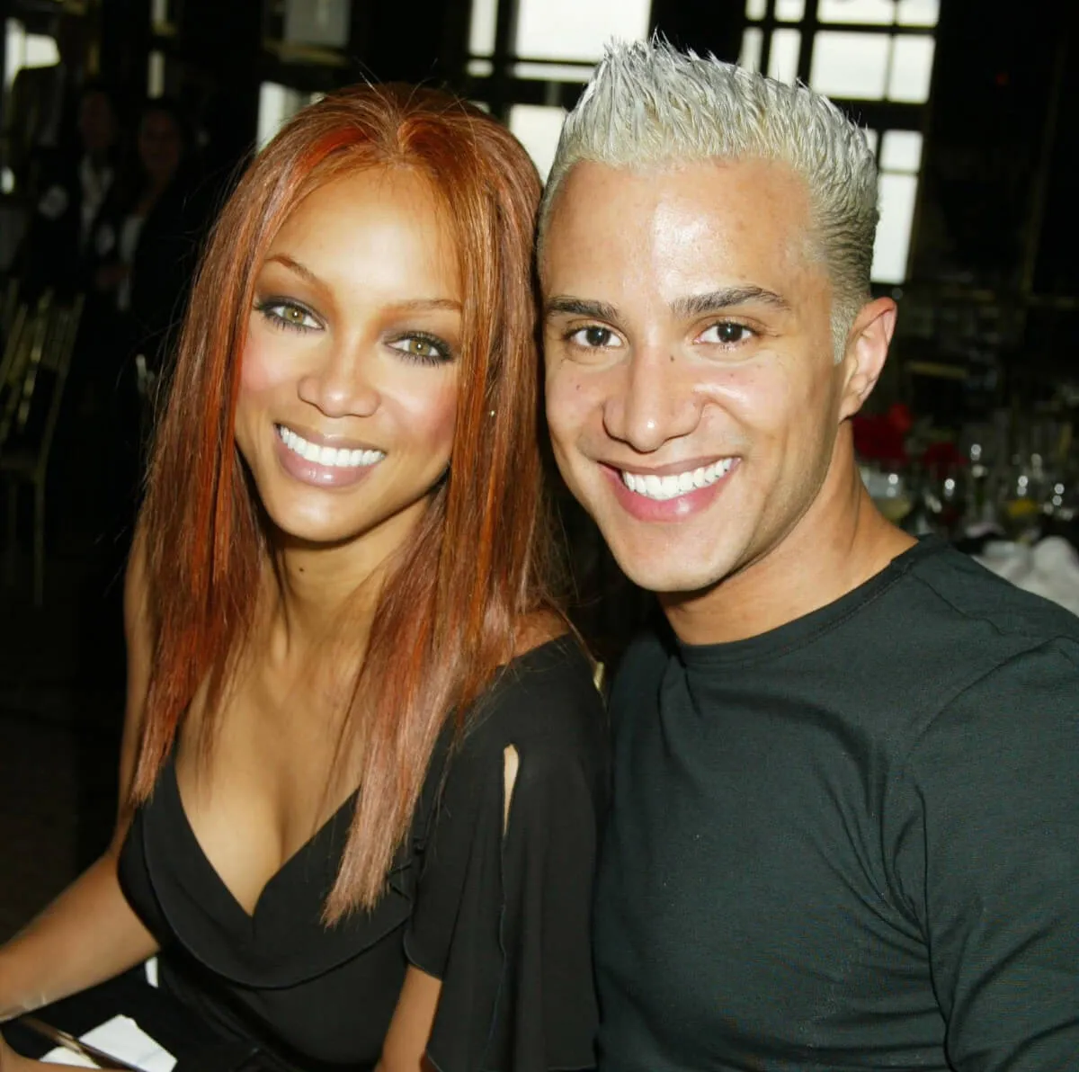 Tyra Banks wears a black shirt and sits with Jay Manuel. He wears a black shirt.