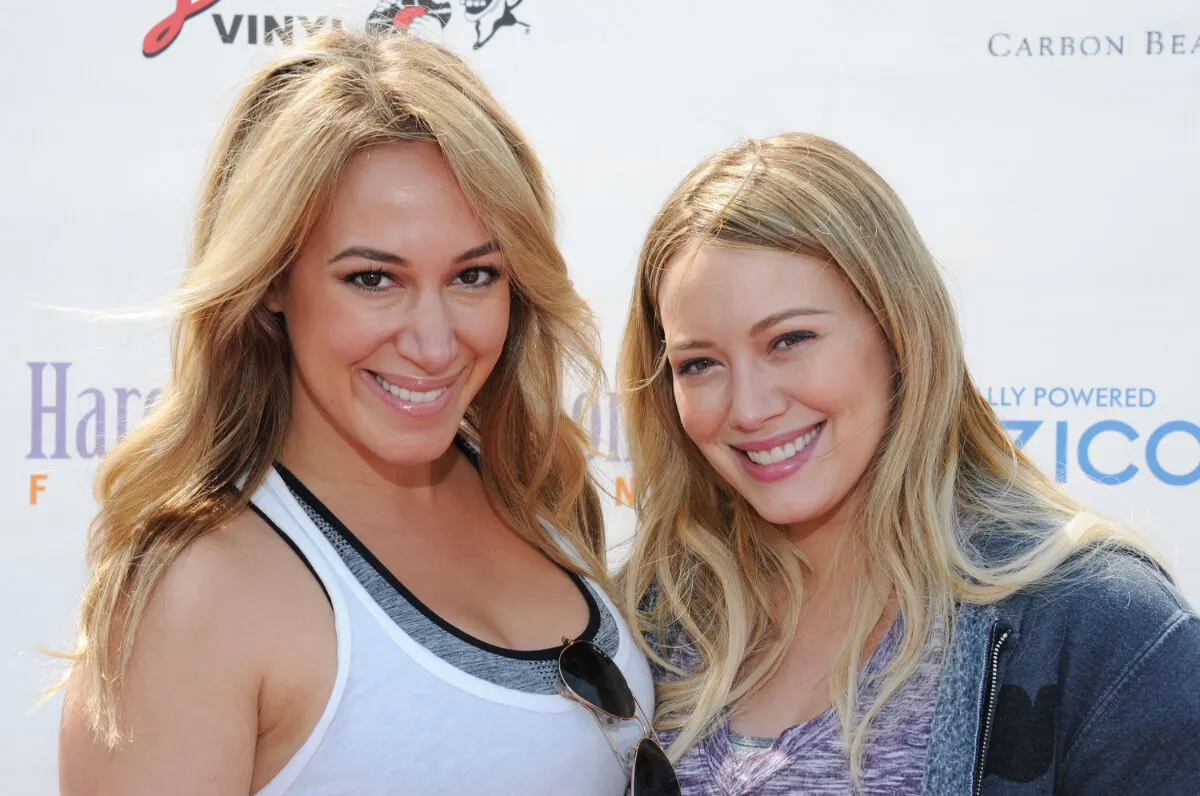 Haylie Duff wears a white tank top and stands with Hilary Duff, who wears a gray hoodie.