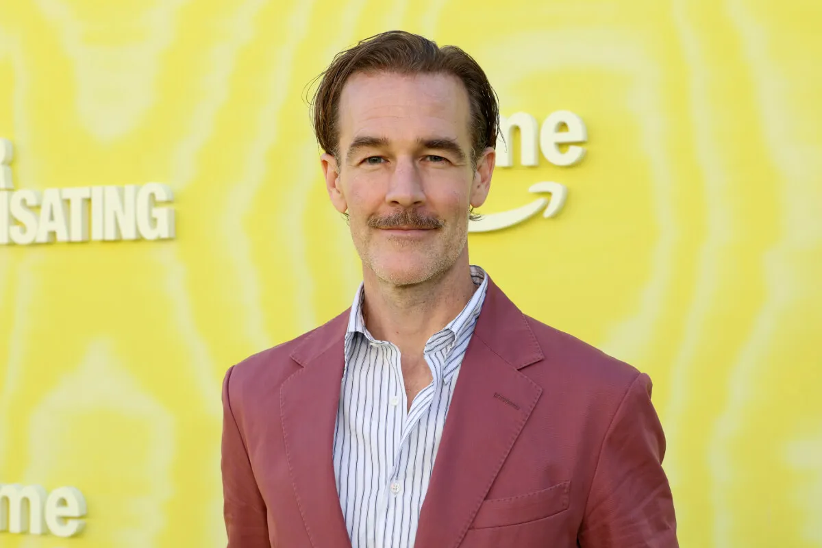 James Van Der Beek wears a pink suit jacket and stands in front of a yellow background.