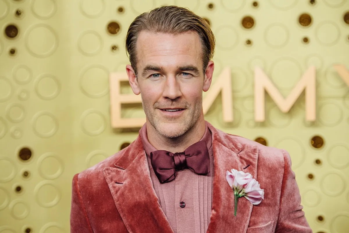 James Van Der Beek in a red suit and a bowtie at the 71st Emmy Awards. He's against a yellow background.