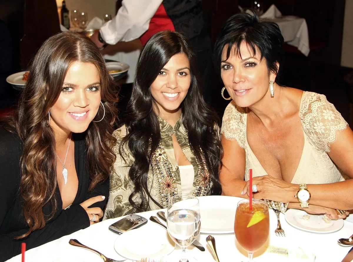 Smiling Khloe Kardashian, Kourtney Kardashian, and Kris Jenner sitting at a table in 2008