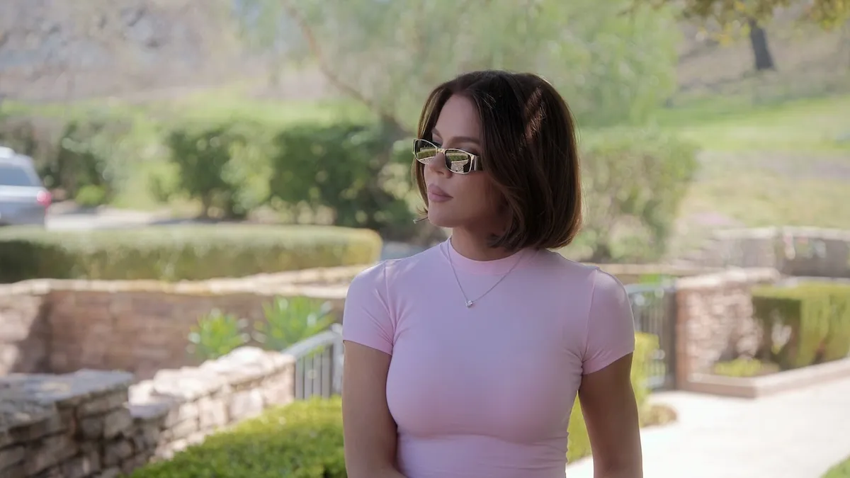 Khloé Kardashian sitting outside in a pink T-shirt and wearing sunglasses on 'The Kardashians'