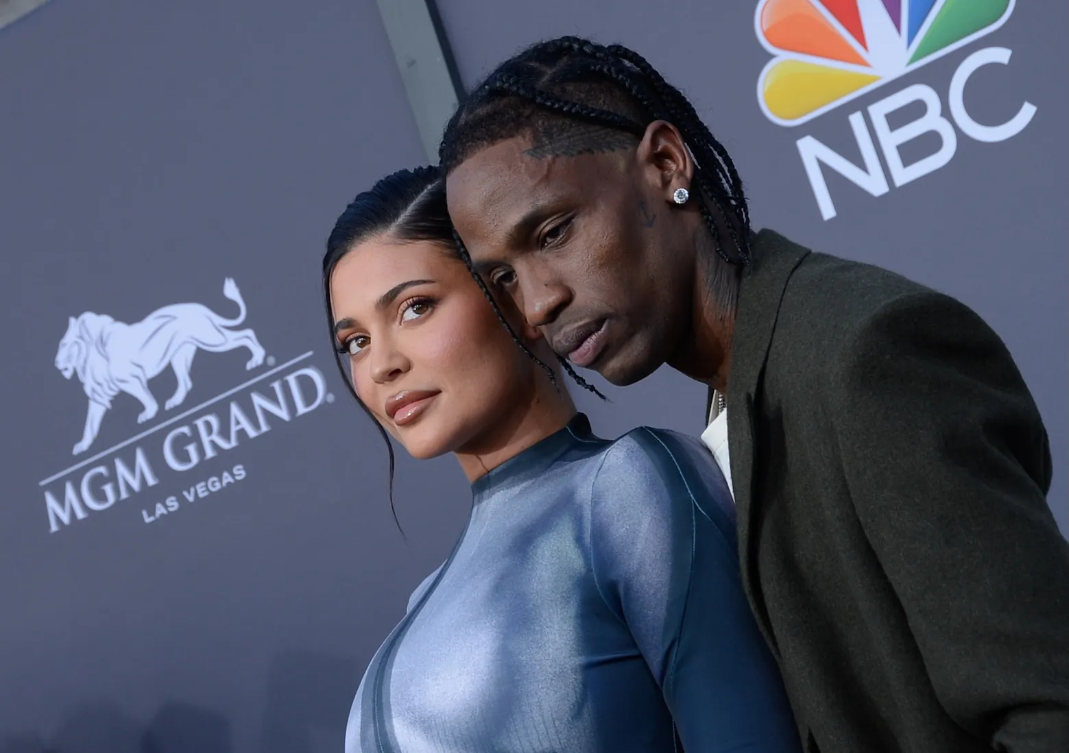 Kylie Jenner in a blue jumpsuit with Travis Scott posing behind her and over a shoulder