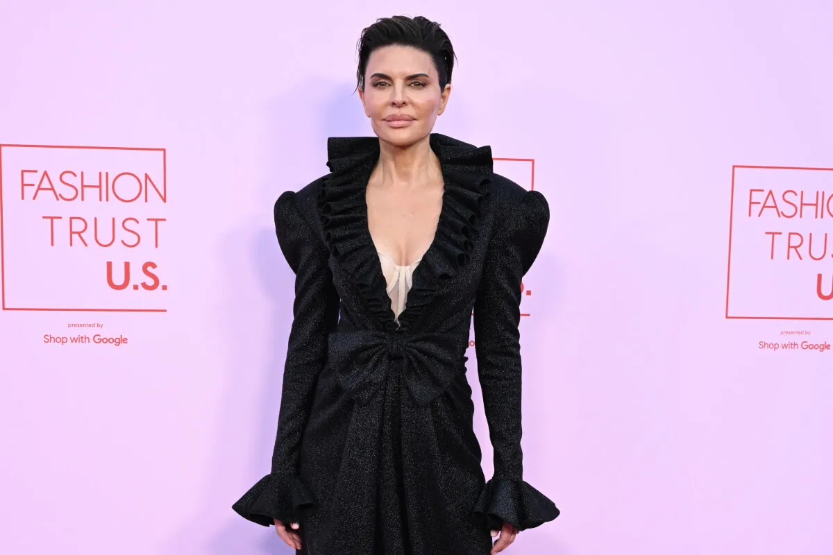 Lisa Rinna wears a black jacket and stands against a lilac background.