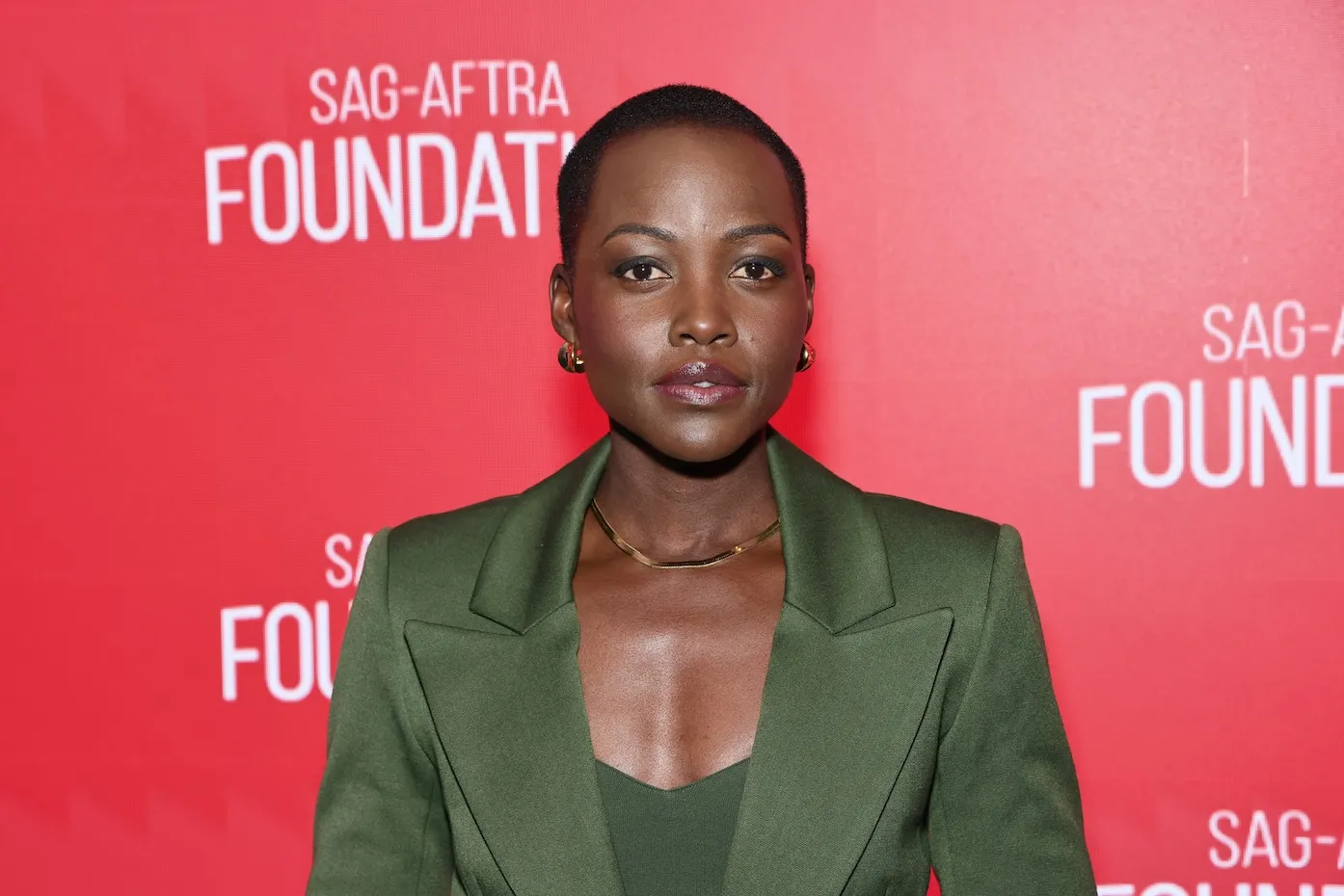 Lupita Nyong'o in a green jacket against a red background