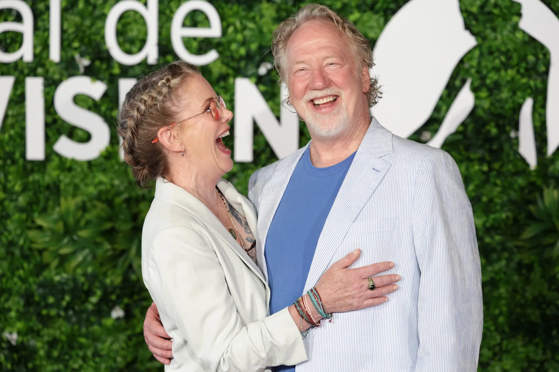 Melissa Gilbert looking at Timothy Busfield excitedly with her mouth open and one arm draped across his front. Busfield is looking ahead with a large smile on his face and one hand on Gilbert's back.