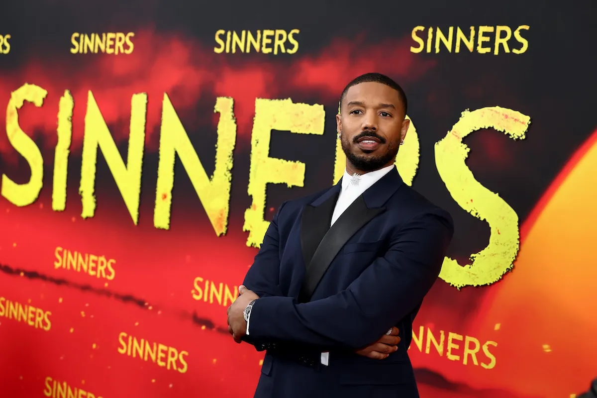 Michael B Jordan standing in front of a large backdrop advertising 'Sinners'