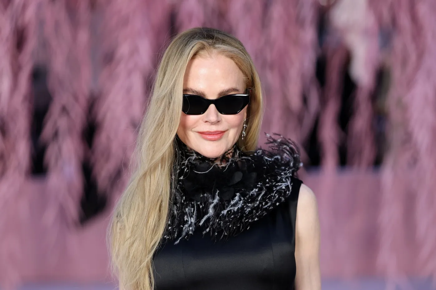Nicole Kidman at Paris Fashion Week in a sleeveless black gown and sunglasses. Her hair is down and cascading over one shoulder.