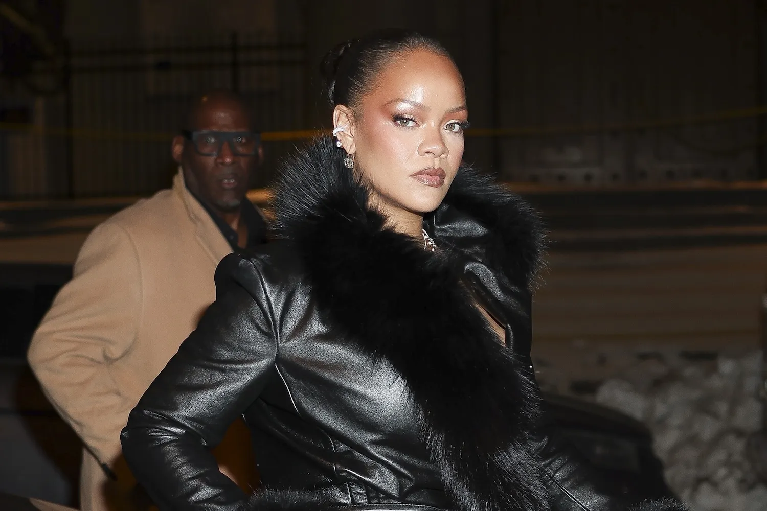 Rihanna at night in a black leather jacket with fur trim.