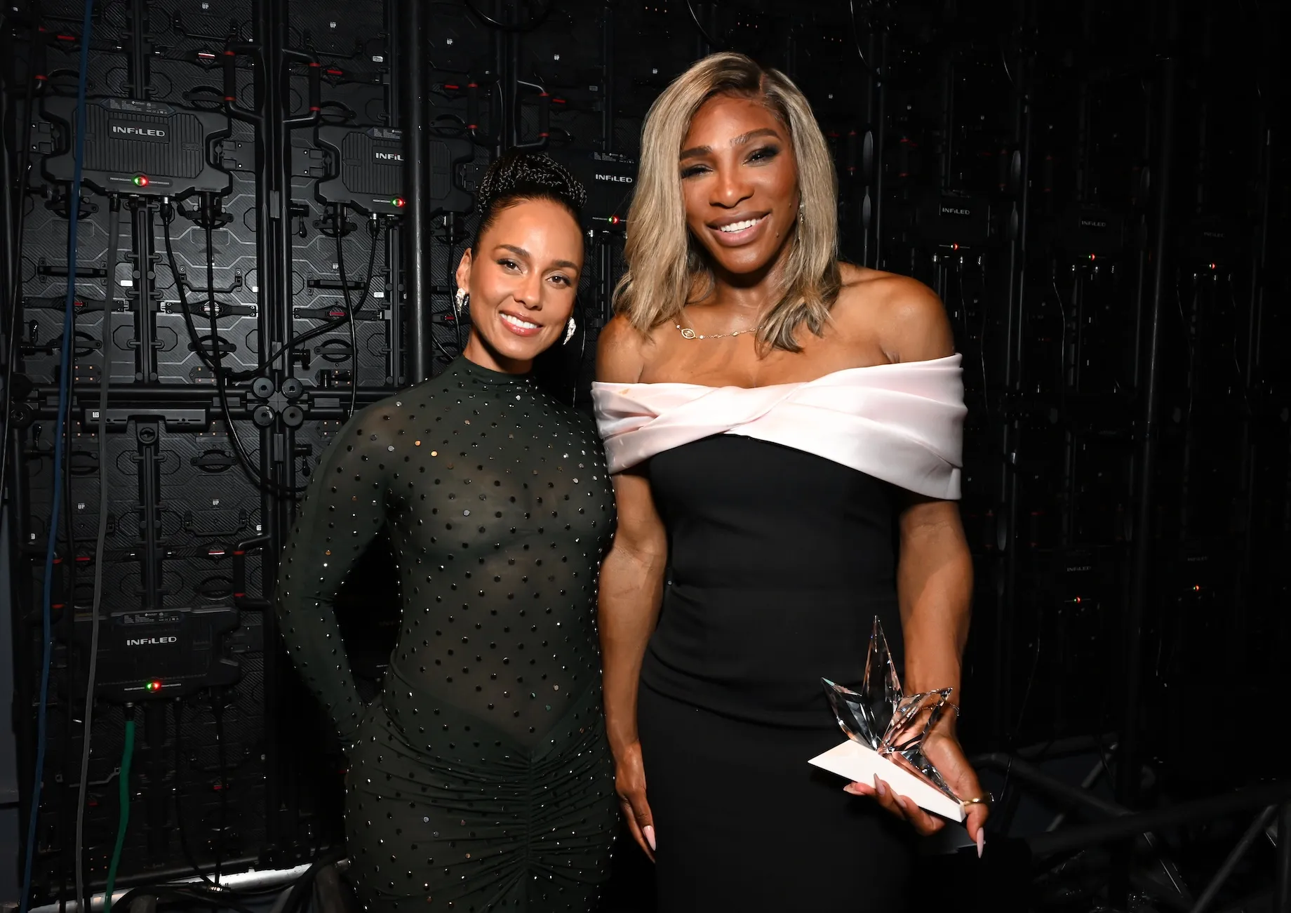 Serena Williams in an off-shoulder black and white gown posing next to Alicia Keys, who's in a long-sleeve black gown
