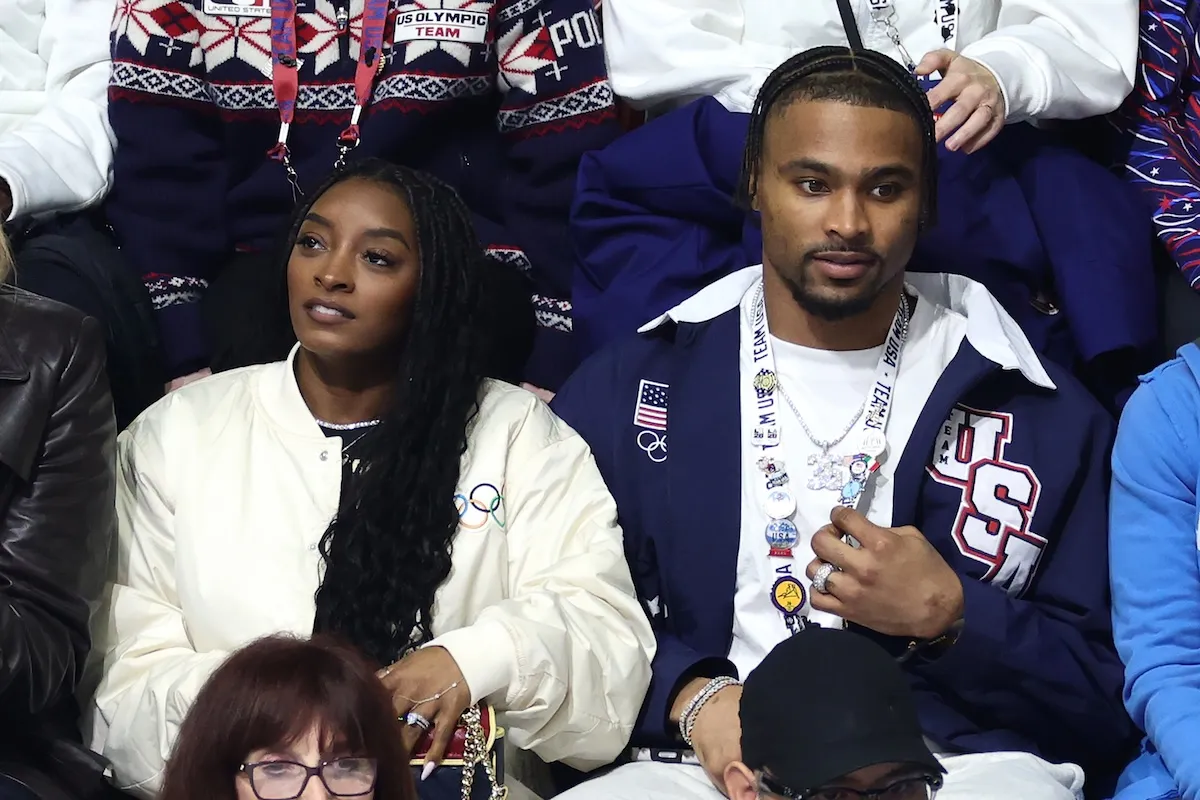Simone Biles and husband Jonathan Owens in attendance at the Men Single Skating at the 2026 Winter Olympics. They're seated together and looking in opposite directions.