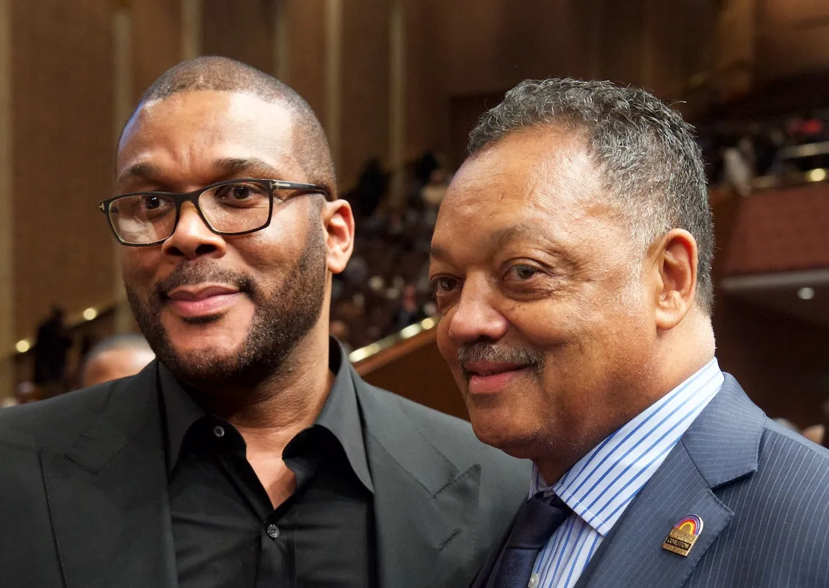 Tyler Perry, wearing round glasses, poses with Rev. Jesse Jackson
