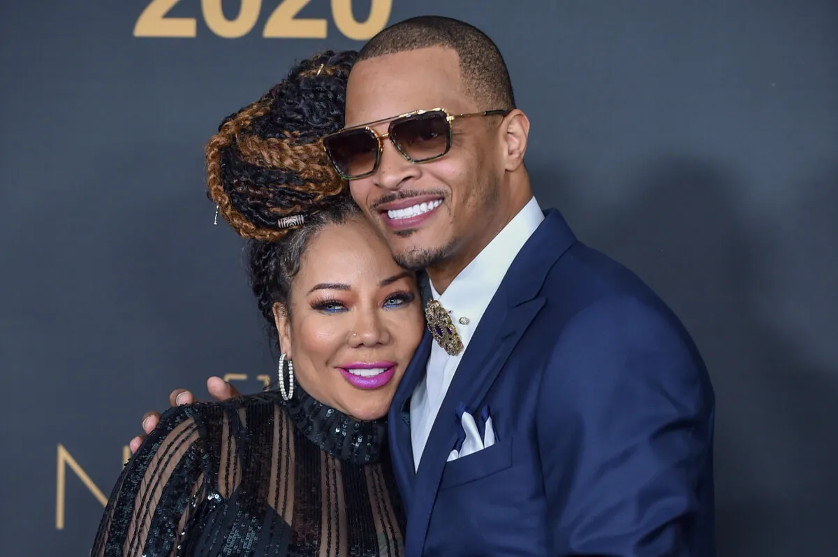 T.I. wears a blue suit and sunglasses and embraces Tiny, who wears black.