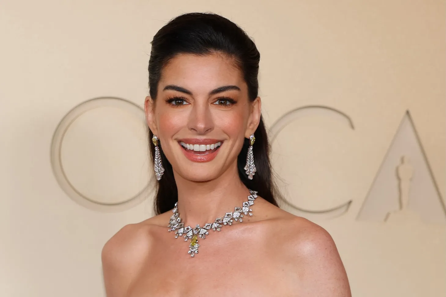 A close-up of Anne Hathaway smiling at the 2026 Oscars