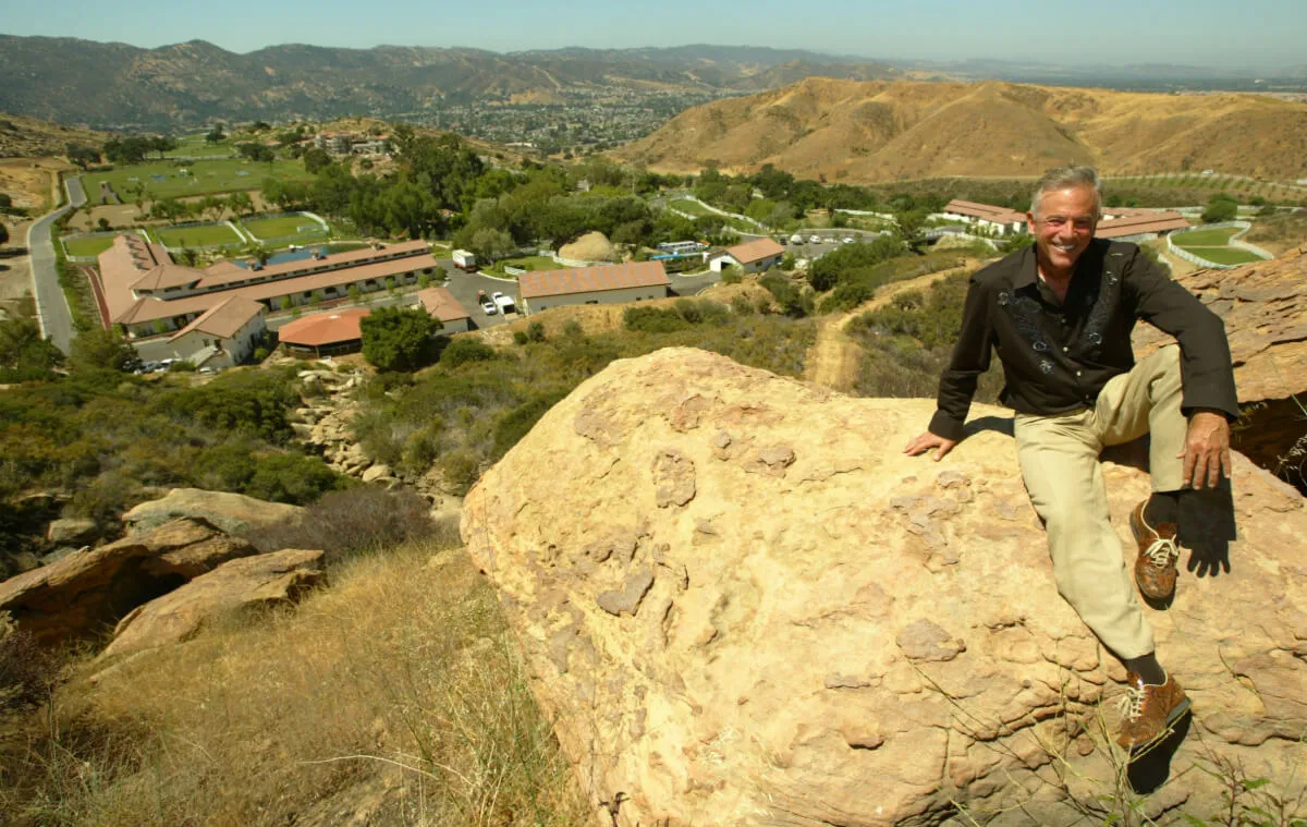 David Saperstein sits on a rock overlooking a mansion.