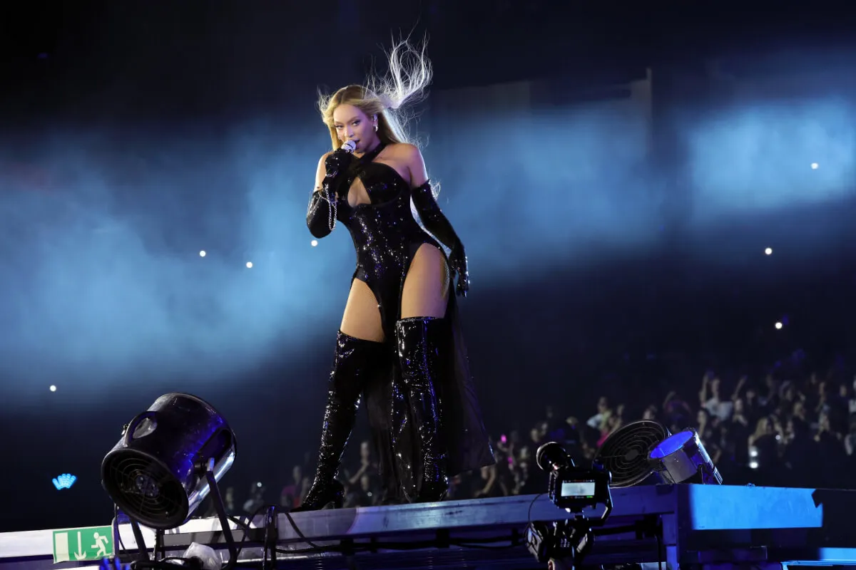 Beyonce wears a black bodysuit and thigh-high heels. She sings into a microphone.