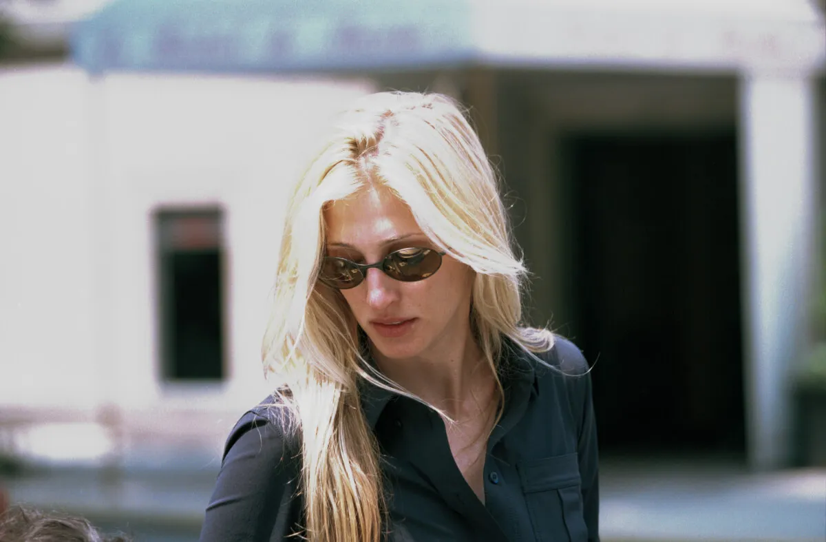 Carolyn Bessette-Kennedy wears sunglasses and a black shirt.