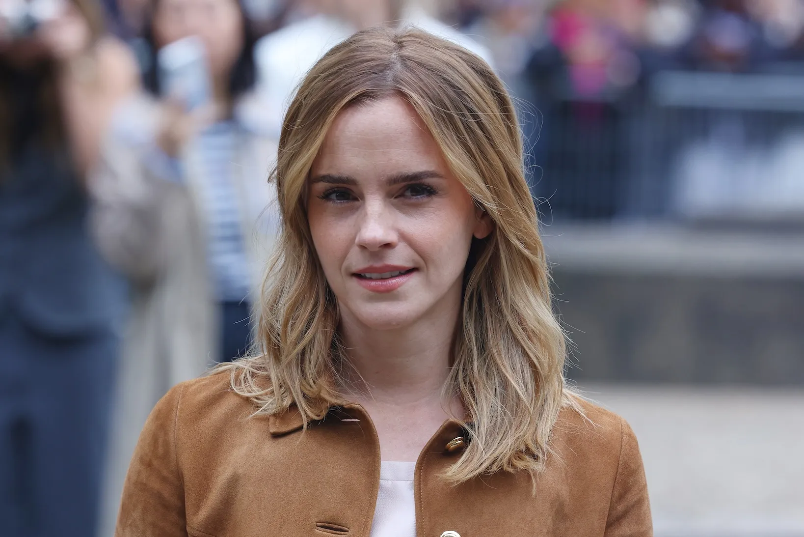 A head shot of Emma Watson on the street. She's wearing a brown jacket and her hair is down.