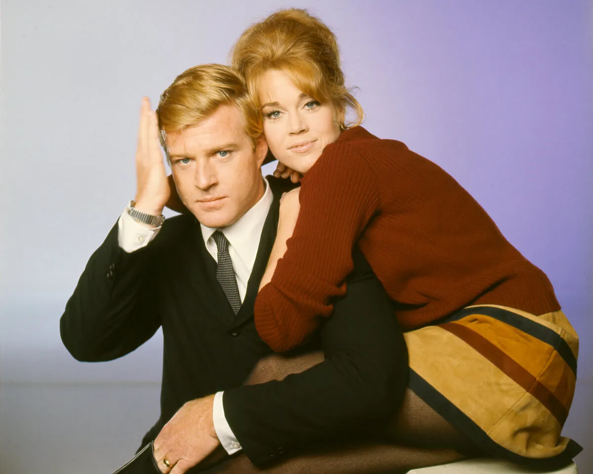 Jane Fonda embraces Robert Redford. He wears a suit and she wears a red sweater and striped skirt.