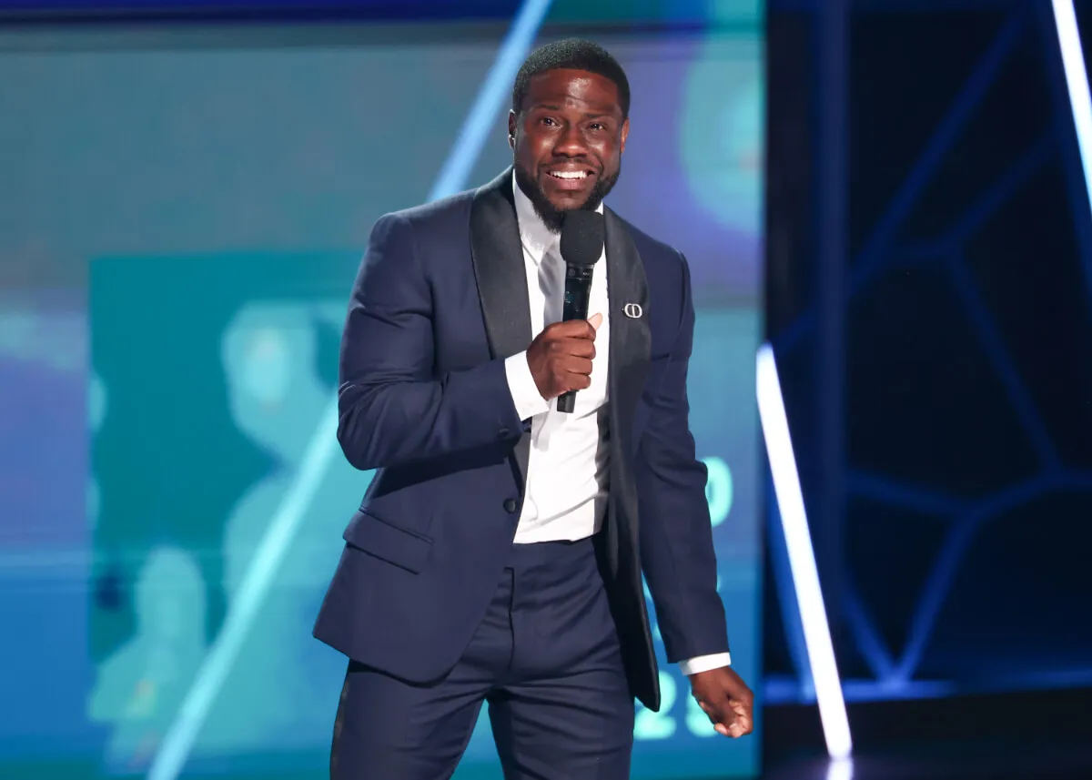 Kevin Hart wears a blue suit and speaks into a microphone.