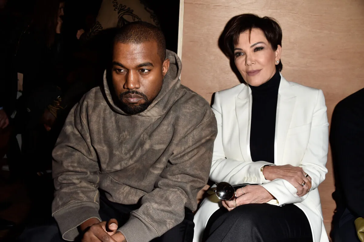 Kanye West wears a hoodie and sits next to Kris Jenner. She wears a black turtleneck and white blazer.