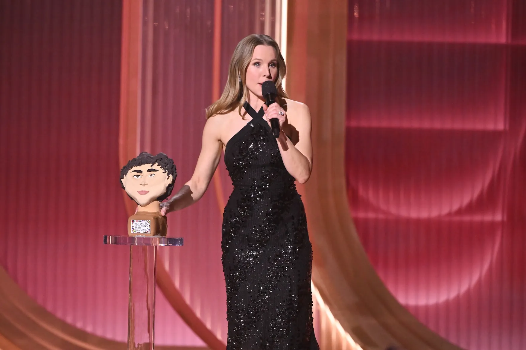 Kristen Bell in a black dress against a red background at the Annual Actor Awards