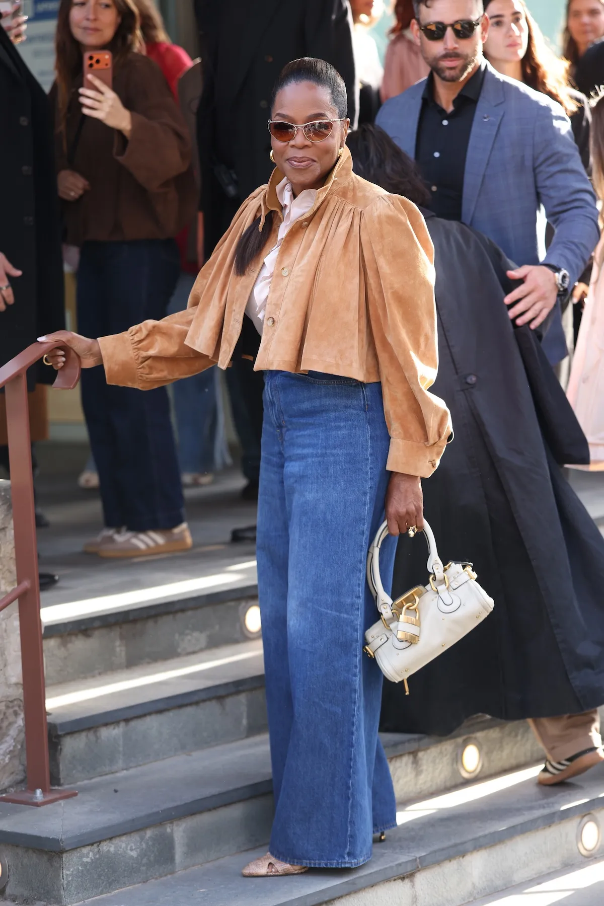 Oprah Winfrey at Paris Fashion Week in 2026. She's outside and wearing a suede jacket with jeans.