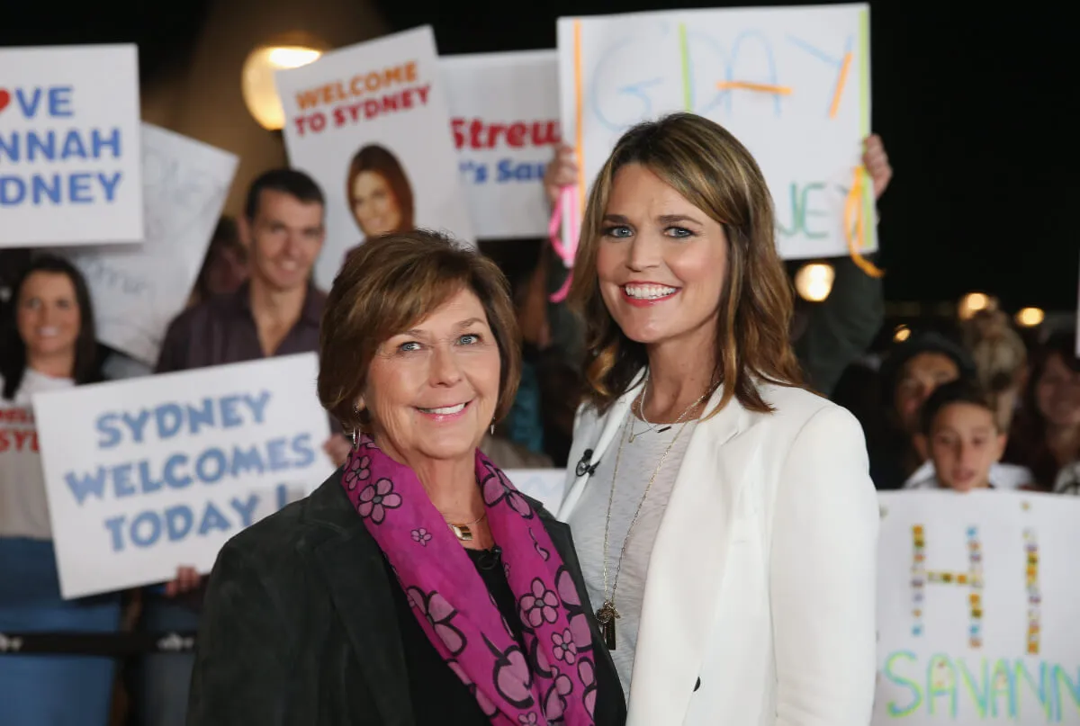 Nancy Guthrie wears a purple scarf and stands with Savannah Guthrie. She wears a white blazer.