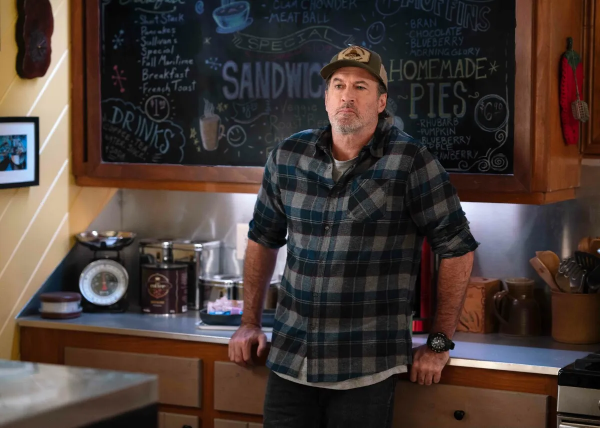 Scott Patterson in a plaid shirt leaning against a counter in 'Sullivan's Crossing'