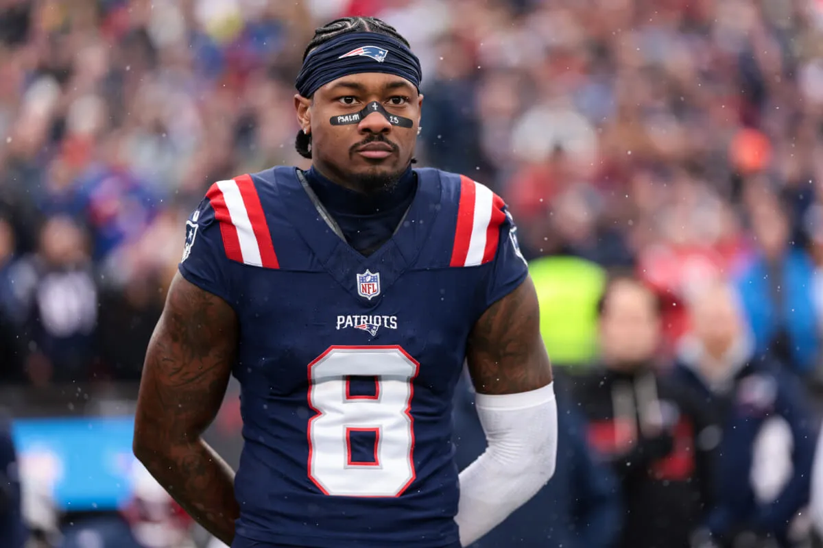 Stefon Diggs wears his Patriots uniform and stands with his arms behind his back. He is on the football field.
