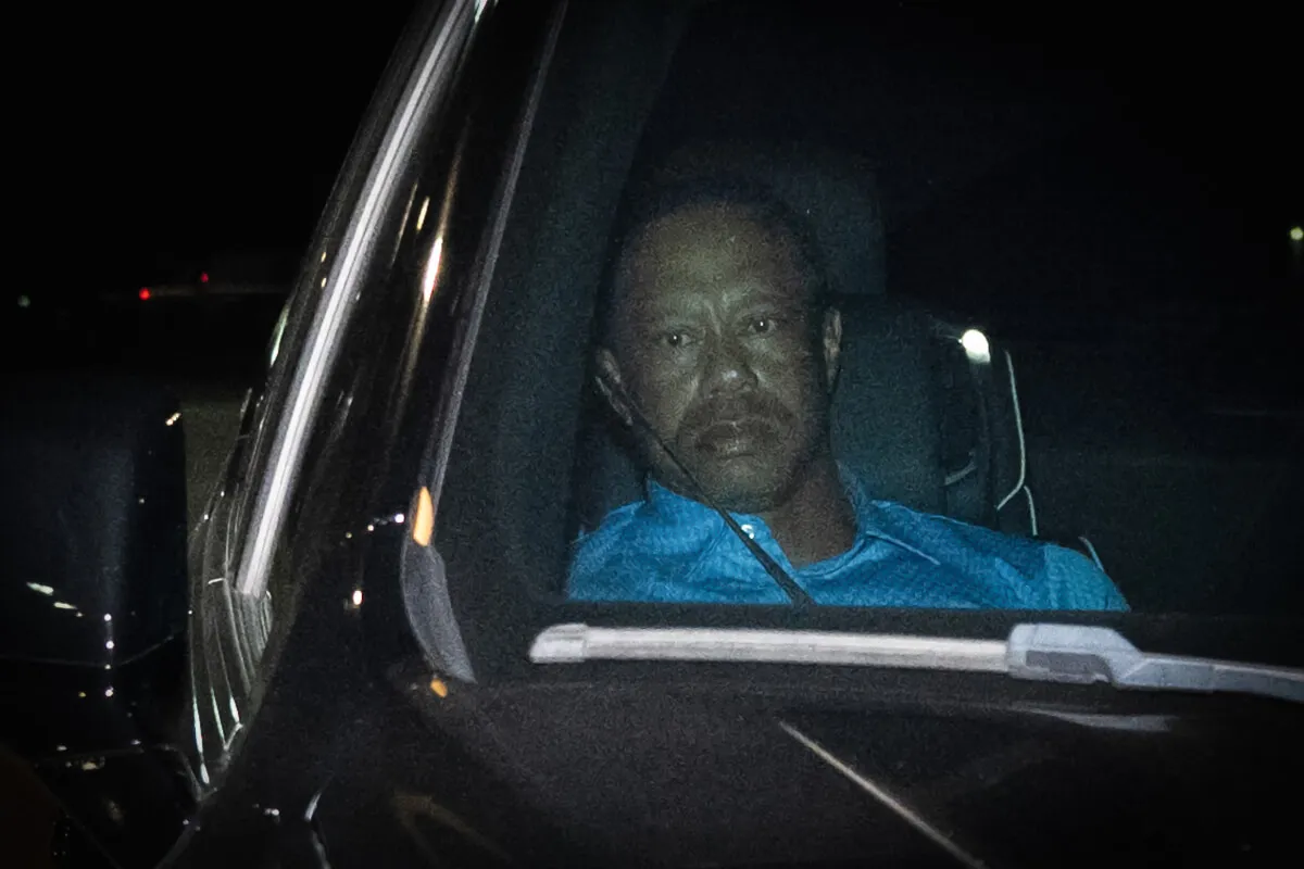 Tiger Woods wears a blue shirt and sits in a car.