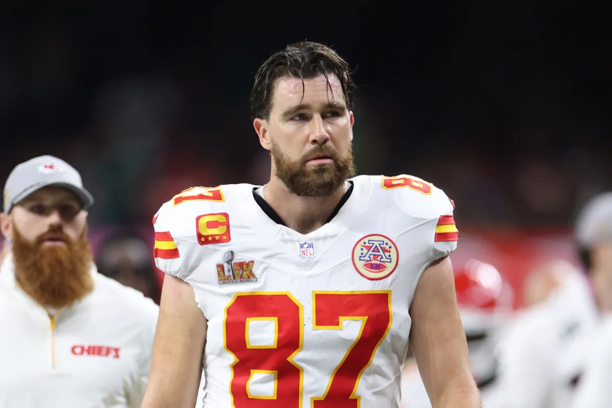 Travis Kelce wears his Kansas City Chief's uniform. He stands on the field.