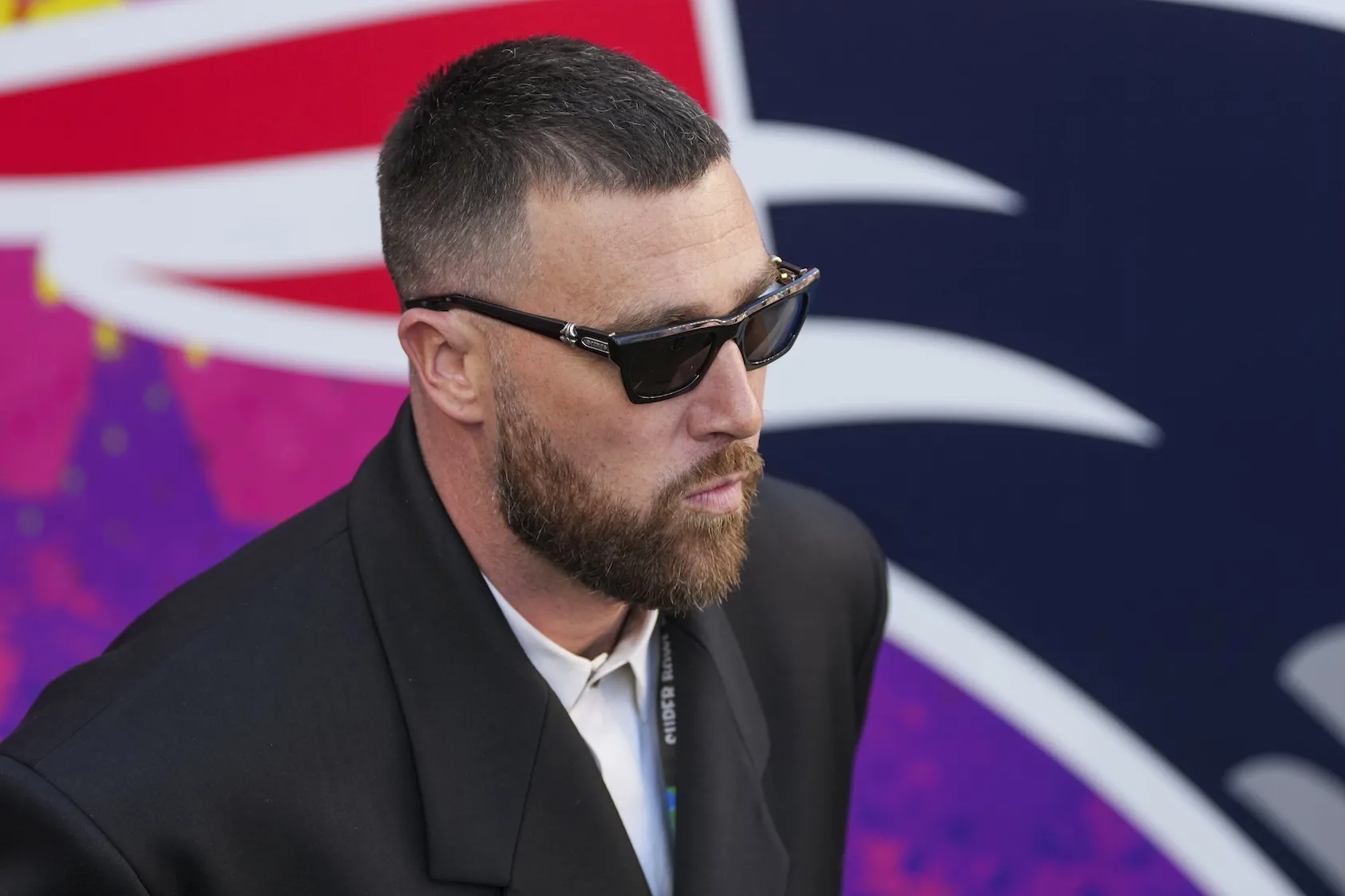 Travis Kelce of the Kansas City Chiefs walks up before the NFL Super Bowl LX football game. He's wearing a suit jacket and sunglasses.