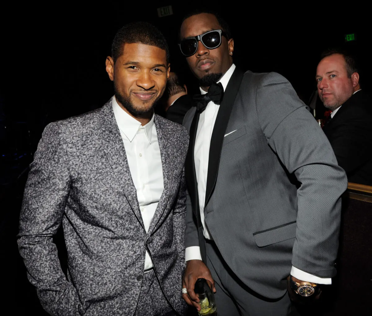 Usher wears a gray blazer and stands with Sean 'Diddy' Combs, who wears a gray tuxedo and sunglasses.