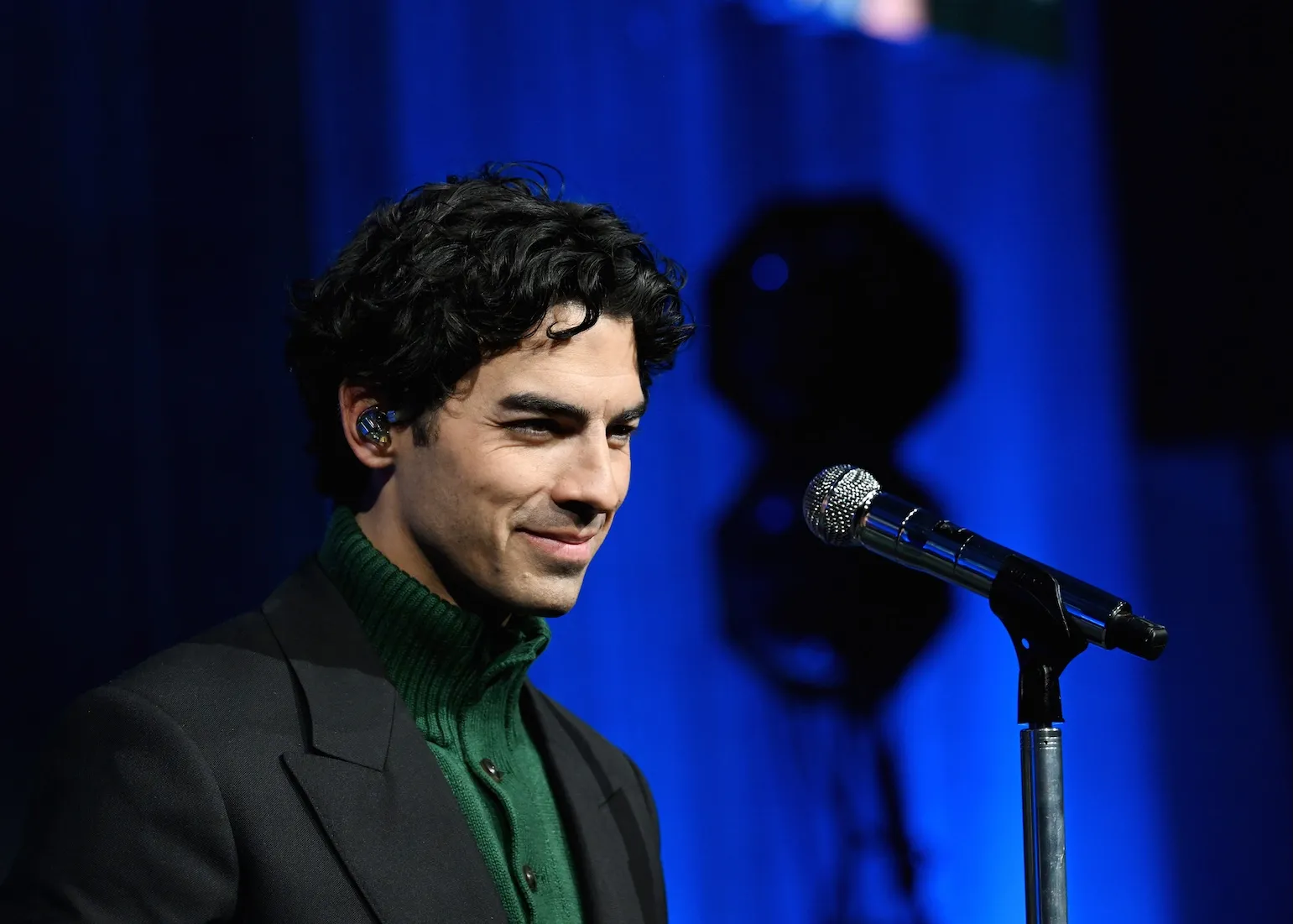 A side view of Joe Jonas slightly smiling against a blue background
