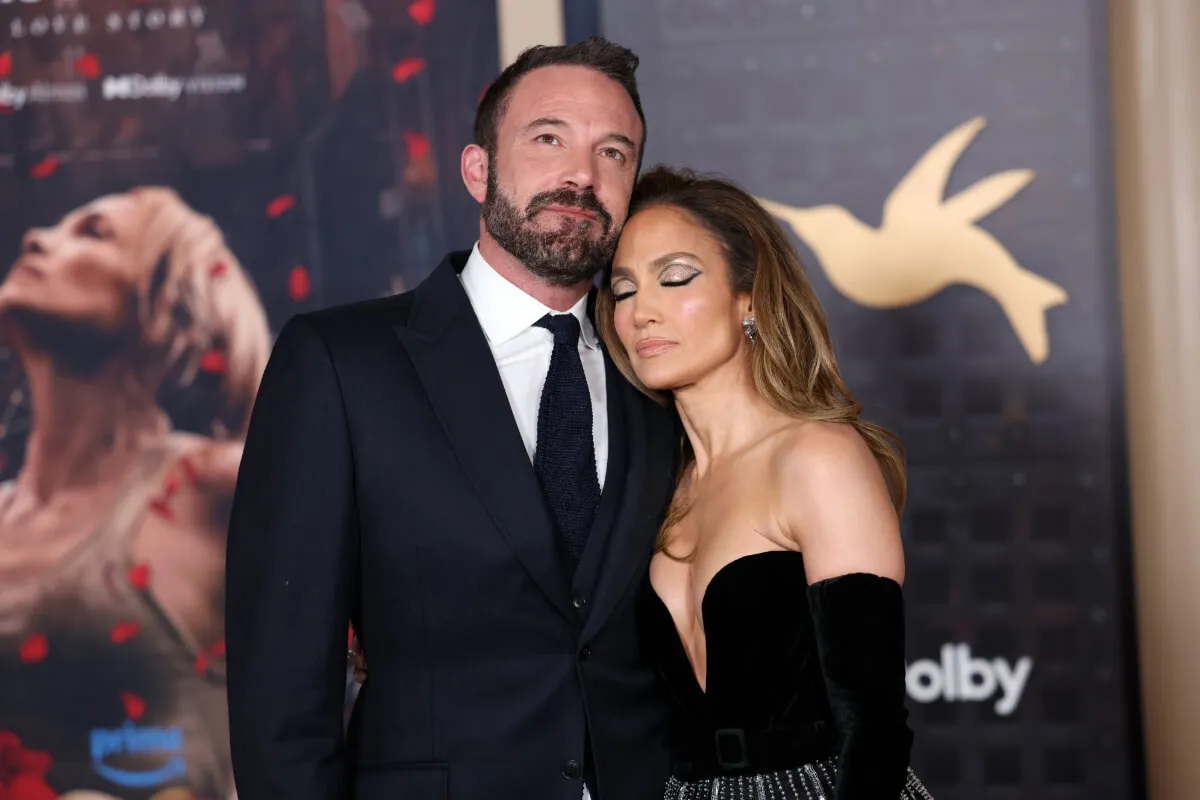 Ben Affleck wears a suit and stands with Jennifer Lopez. She wears a black strapless dress and black gloves. Her eyes are closed.